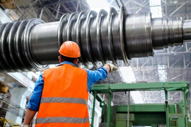 High-performance turbine shaft being inspected by an engineer in an industrial factory setting.