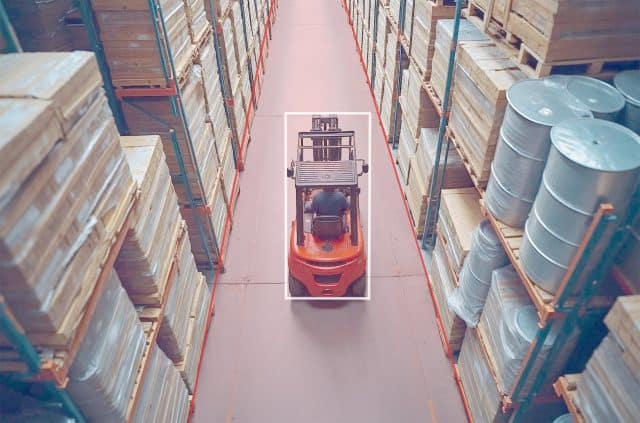 Forklift navigating warehouse storage racks with wood and metal barrels.