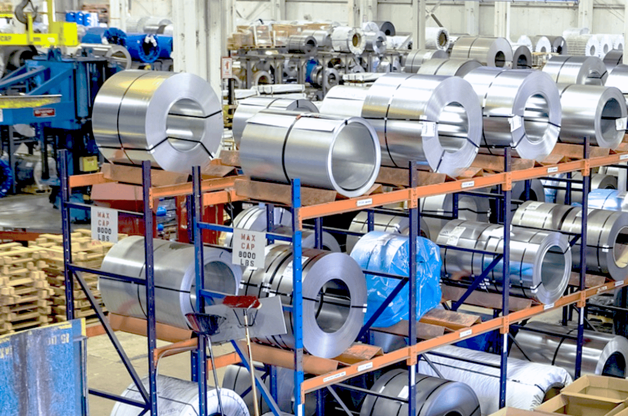 Shiny steel coils stacked on industrial metal racks in factory warehouse.
