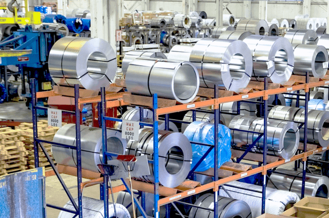 Shiny steel coils stacked on industrial metal racks in factory warehouse.