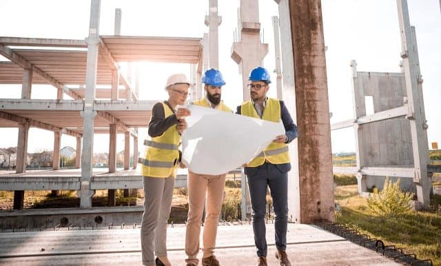 Blue hard hats and high-visibility vests inspecting construction site blueprints on a building project.
