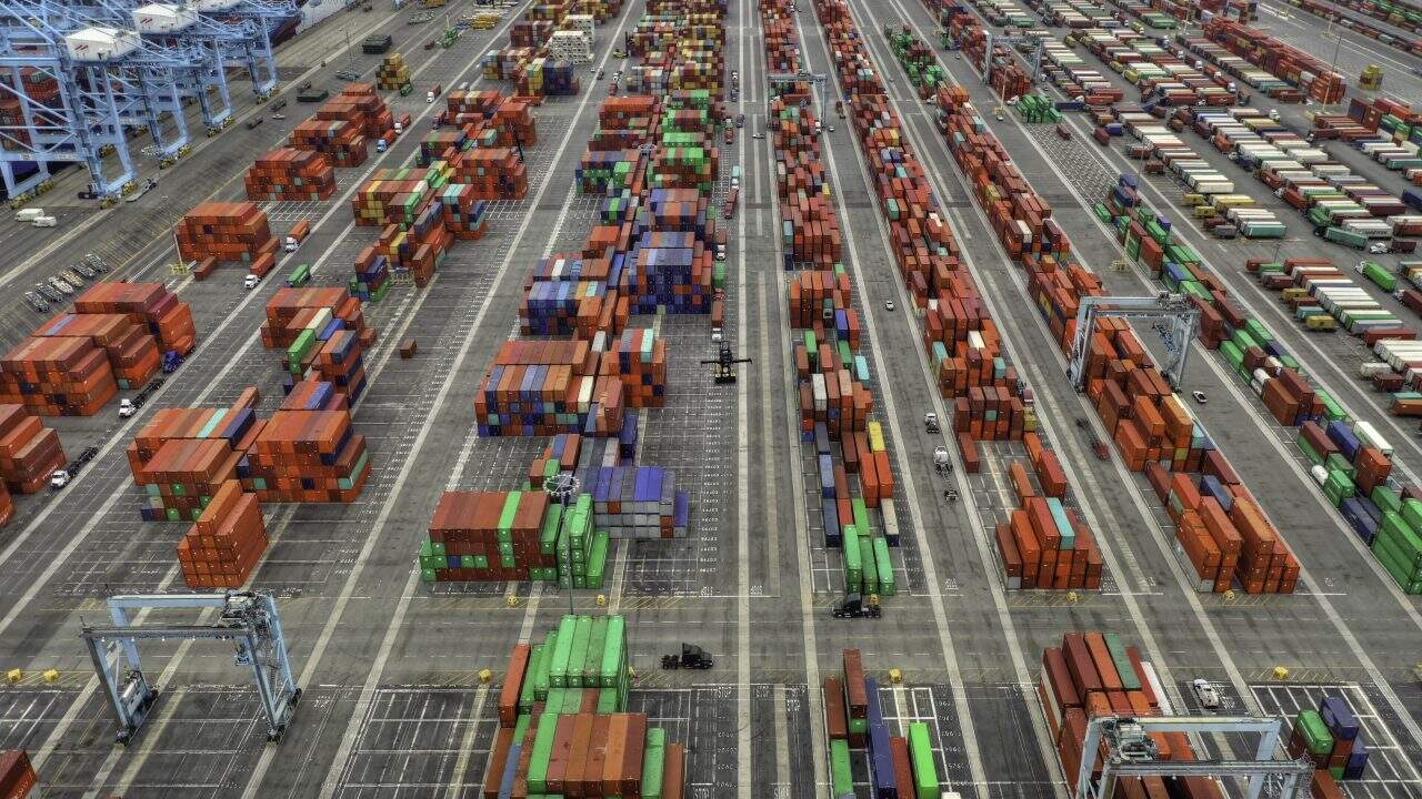 Containers stacked at a busy shipping port with cranes and trucks for logistics and freight management.